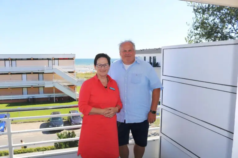 Eine Frau und ein Mann stehen auf einem Balkon mit Meer im Hintergrund
