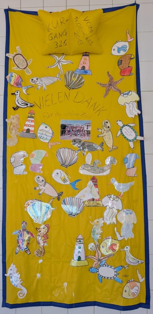 Ein selbstgebasteltes Abschiedsgeschenk welches ein gelbes Strandtuch mit blauem Rand und vielen Meereslebewesen darauf zeigt.